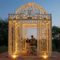 Digital representation of "The Royal Alexandria" Cream Wrought Iron Gazebo lit up with fairy lights at night
