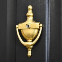 Polished Brass Urn door knocker with security viewer on black door Polished Brass Urn door knocker with security viewer on black door