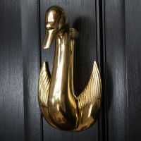 Swan door knocker mounted on black door Swan door knocker mounted on black door