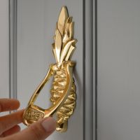 Pineapple door knocker on a grey door with hand