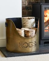The Set of Two "LOGS" and "KINDLING" buckets in an Antique Brushed Gold Finish next to a Lit Log Burner Stove - Digital Illustration