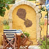 Floating House on Balloons Steel Wall Art on a Yellow Brick Wall in a Garden
