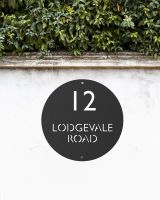 Modern Circular Steel House Sign on a White Garden Wall