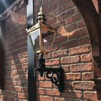 Polished Brass Harrogate Wall Lantern on Bracket Mounted on a Brick Wall in the Garden