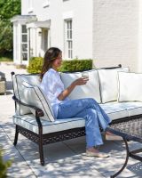 Scale shot showing a person sat on sofa, part of the "Elmswood" five seater garden furniture set.