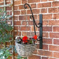 Black Scrolled Hanging Basket Bracket Holding a Flower Basket in the Garden Black Scrolled Hanging Basket Bracket Holding a Flower Basket in the Garden