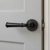 The Edlyn House Midnight Black Unsprung Lever Door Handle on Rose on a Light Grey Door in a Modern Interior Setting - Digital Illustration