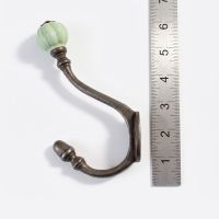 The Ironmonger Acorn Light Green Ceramic Coat Hook - 125mm on a White Background next to a Steel Ruler for Scale - Digital Illustration