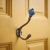 The Ironmonger Acorn Sky Blue Ceramic Coat Hook - 125mm Shown Close up on a Yellow Door - Digital Illustration
