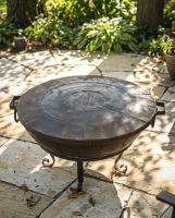 The Kadai Fire Bowl Shield and Snuffer Lid Shown on top of a Raised Fire Bowl on a Sunny Garden Patio - Digital Illustration