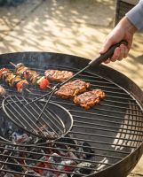 The Kadai Iron Grill Lifter with Hardwood Handle Shown Being used to Lift a Grill on a Fire Pit - Digital Illustration