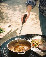 The Kadai Long-Handled Iron Cooking Ladle with Wooden Grip Shown being used over a Lit Kadai Bowl - Digital Illustration