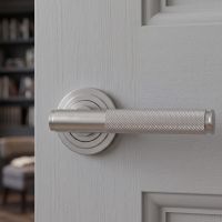 The Knurled Sprung Handle Set on an Art Deco Rose in Satin Stainless Steel Shown Close up on an Open Door Leading to a Living Room - Digital Illustration