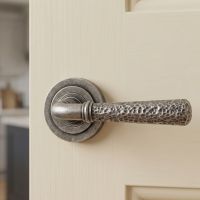 The Landen House Aged Pewter Hammered Unsprung Lever Door Handle on Art Deco Rose Shown Close up on an Open White Door - Digital Illustration