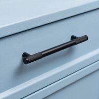The Medium Half Knurled Cabinet Pull Handle in Matt Black on a Light Blue Set of Drawers in a Modern Home - Digital Illustration