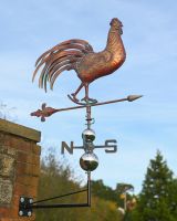 The Proud Cockerel Verdigris Copper Weathervane Mounted on a Red Brick Wall