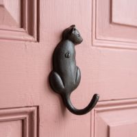 The Seated Cat Antique Iron Coat Hook - 125mm Shown Mounted on the Back of a Pink Door - Digital Illustration
