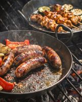 The Set of 3 Kadai Iron BBQ Skillet Pan Set Showing a Close up of Sausages and Skewers Cooking on the Skillets - Digital Illustration