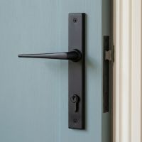 The Slimline Lever Espagnolette Door Latch in Aged Bronze Mounted onto a Light Blue Door in a Modern Home - Digital Illustration