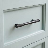 The Small Half Knurled Cabinet Pull Handle in Aged Bronze Displayed on a Sage Green Wooden Drawer in a Modern Interior - Digital Illustration
