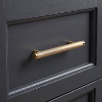 The Small Knurled Cabinet Pull Handle in Polished Brass Shown on a Dark Grey Kitchen Drawer - Digital Illustration