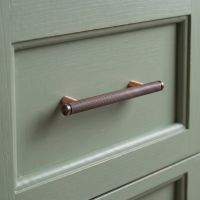  The Small Knurled Cabinet Pull Handle in Polished Bronze Mounted onto a Light Green Set of Drawers in a Kitchen Interior - Digital Illustration
