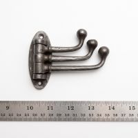 The Swivel Triple Arm Cast Iron Coat Hook 75mm x 100mm on a White Background next to a Steel Ruler for Scale - Digital Illustration