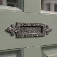 The 14¼" Antique Black Iron Fleur-De-Lys Inspired Door Letter Plate on a Sage Green Door to a Period Home - Digital Illustration