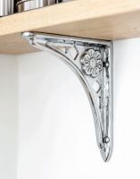 The 15cm x 15cm Tudor Rose Bright Chrome Shelf Bracket Mounted on a White Coloured Wall Supporting a Wooden Shelf - Digital Illustration 