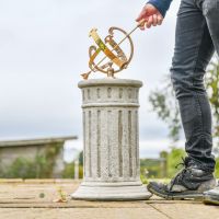 The 17cm "Profatius" Antique Brass Armillary on a Grey Stone Pillar with Hand in Shot for Scale The 17cm "Profatius" Antique Brass Armillary on a Grey Stone Pillar with Hand in Shot for Scale
