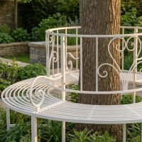 The "Averley" Circular Wrap-Around Garden Tree Bench in a Cream Finish Shown in a Sunny Garden Around the Base of a Tree Looking Close up at the Left Side- Digital Illustration The "Averley" Circular Wrap-Around Garden Tree Bench in a Cream Finish Shown in a Sunny Garden Around the Base of a Tree Looking Close up at the Left Side- Digital Illustration