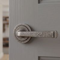 The "Barnsley" Pewter Round Lever Door Handle on Art Deco Rose Fitted onto a Light Grey Door in a Country Home - Digital Illustration 
