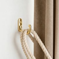 The "Castleford" Curtain Tie Back Hook Mounted on a White Interior Wall Holding a Curtain Back - Digital Illustration