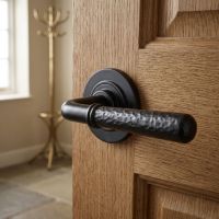 The "Franbury" Black Hammered Lever Door Handle on Rose on a Wooden Door in a Home Entrance with Coat Stand - Digital Illustration
