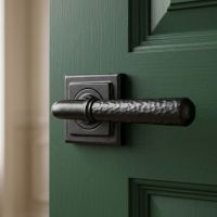 The "Hunter Lodge" Midnight Black Hammered Unsprung Lever Door Handle on Square Rose on a Green Door in a Cream Coloured Interior - Digital Illustration
