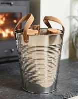 The "Kinsbury" Ribbed Stainless Steel Log Holder in a Modern Living room in Front of a Lit Log Burner Stove - Digital Illustration