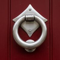 The "Lorien" Ring Door Knocker in Satin Stainless Steel Shown Front on Mounted to a Red Door - Digital Illustration