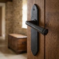 The "Orelia" Beeswax Gothic Latch Lever Set on a Heavy Timber Door in a Cottage Home - Digital Illustration