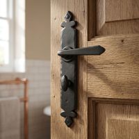 The "Vittoria" Black Tudor Sprung Lever Bathroom Privacy Set Shown on a Timber Door with a Brass Towel Rail Behind - Digital Illustration