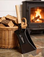 The 23cm Traditional Coal Shovel With Light Wood Handle Displayed in Front of a Lit Fire Place on a Stone Tiled Floor - Digital Illustration