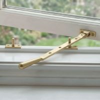 The 296mm 10" Satin Brass Four Pin Window Stay Mounted on a White Window Frame in a Modern Home - Digital Illustration
