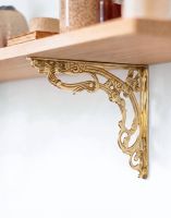 The 30 x 25cm Ornate “Victorian Amalina” Scroll Bracket in Polished Brass Mounted on a Bright white Coloured Modern Interior Wall on a DIY Shelf - Digital Illustration
