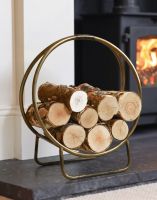 The 45cm Antique Brass Contemporary Circular Log Rack & Holder With Handle on a Black Stone Fireplace next to a Log Burner - Digital Illustration The 45cm Antique Brass Contemporary Circular Log Rack & Holder With Handle on a Black Stone Fireplace next to a Log Burner - Digital Illustration