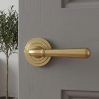 The 53mm Modern Satin Brass "Neville" Unsprung Art-Deco Door Handle on Rose Set on a Light Grey Door in a Clean and Modern Interior Setting - Digital Illustration 