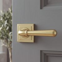The 53mm Modern Satin Brass "Neville" Unsprung Door Handle on Square Rose Set on a Light Grey Door in a Modern Home - Digital Illustration