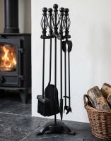 The 66cm Classic Black Iron Companion Set with Basket Handles next to a Traditional Log Burner Stove - Digital Illustration