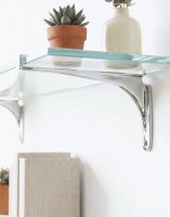 The 9cm x 18cm Kelsall" Bright Chrome Glass Shelf Bracket Mounted on a White Wall in a Modern Living Room - Digital Illustration