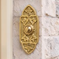 The "Adie Amus" Polished Brass Antique Gothic Bell Push on a Stone Wall next to a Cream Coloured Front Door - Digital Illustration 