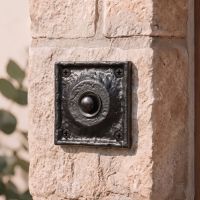 The Antique Black Iron Square Design Front Door Bell Push on a Rose Coloured Stone Wall next to a Front Door - Digital Illustration 