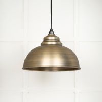 The Arcus Spun Pendant Light in Aged Brass Shown on a White Panelled Background